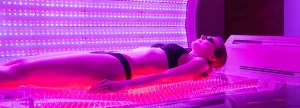 une femme allongée dans une cabine de photobiomodulation corps entiers avec des lumieres rouge qui illumine son corps